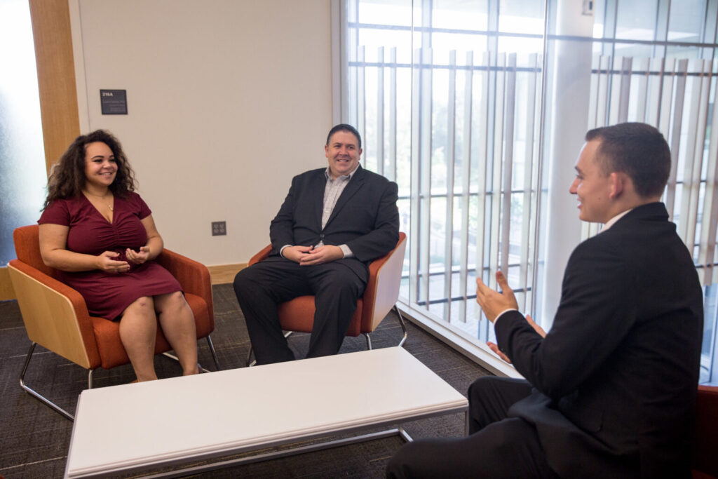 Three MBA students discussing leadership, networking and business strategy in collaborative meeting space.