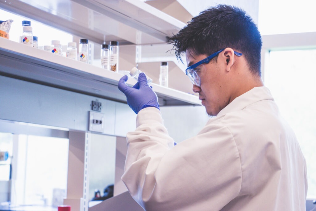 Engineering student wearing a lab coat, goggles, and gloves, doing an experiment in the lab.