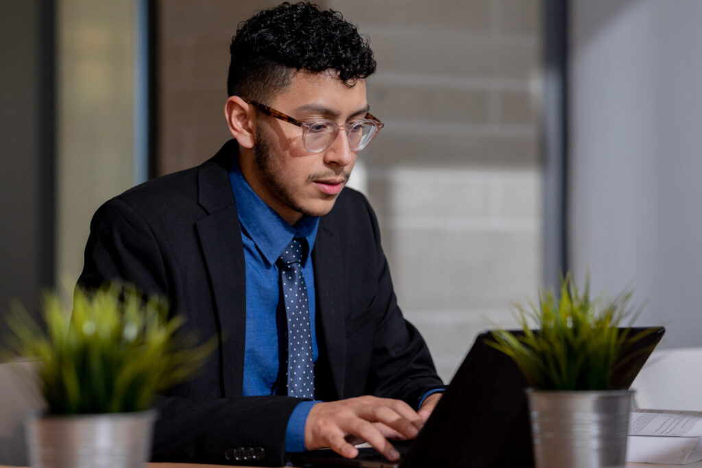 Business professional in blue and black suit working on a laptop while exploring MBA career advancement opportunities in an office setting.