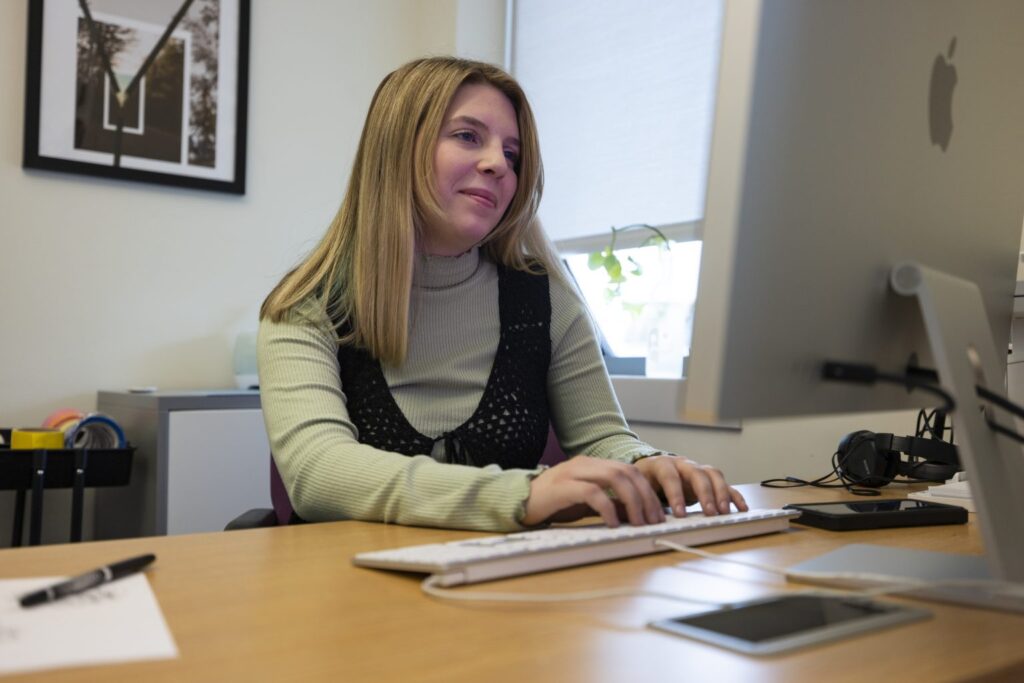 Woman sitting at a desk and working on a desktop computer in an office environment.