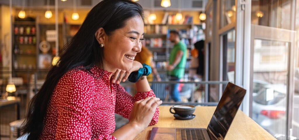 Woman smiling while using a laptop in a café during an online college class.