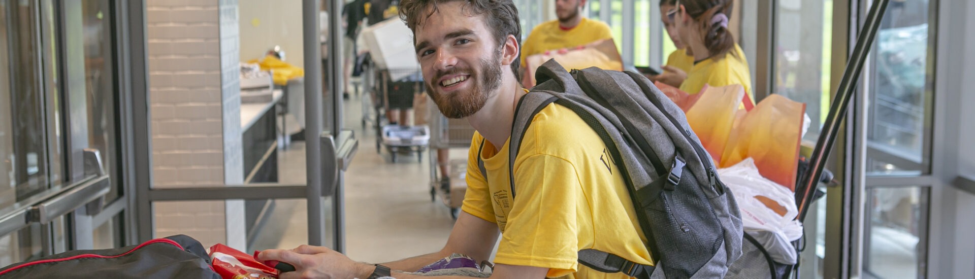 A Rowan University student smiles while pushing a cart filled with dorm supplies through a residence hall during move-in day.