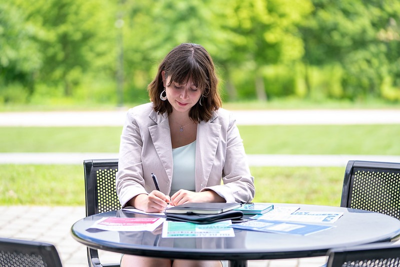 Woman writing in a notebook while seated at an outdoor table.