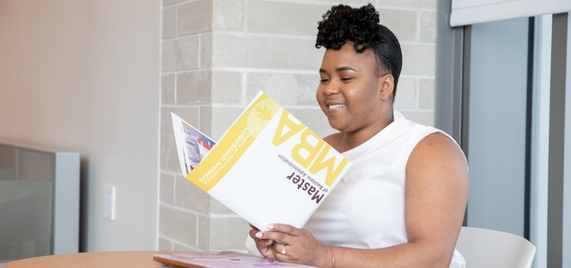 Woman reading an MBA brochure while sitting at a table on campus.