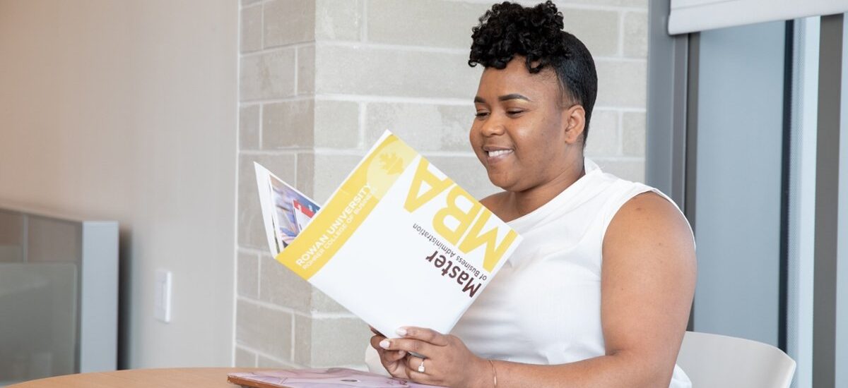 Woman reading an MBA brochure while sitting at a table on campus.