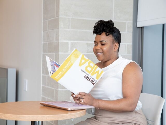 Woman reading an MBA brochure while sitting at a table on campus.