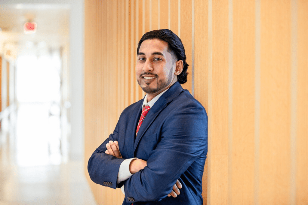 Man in professional business attire standing confidently in a university building hallway.