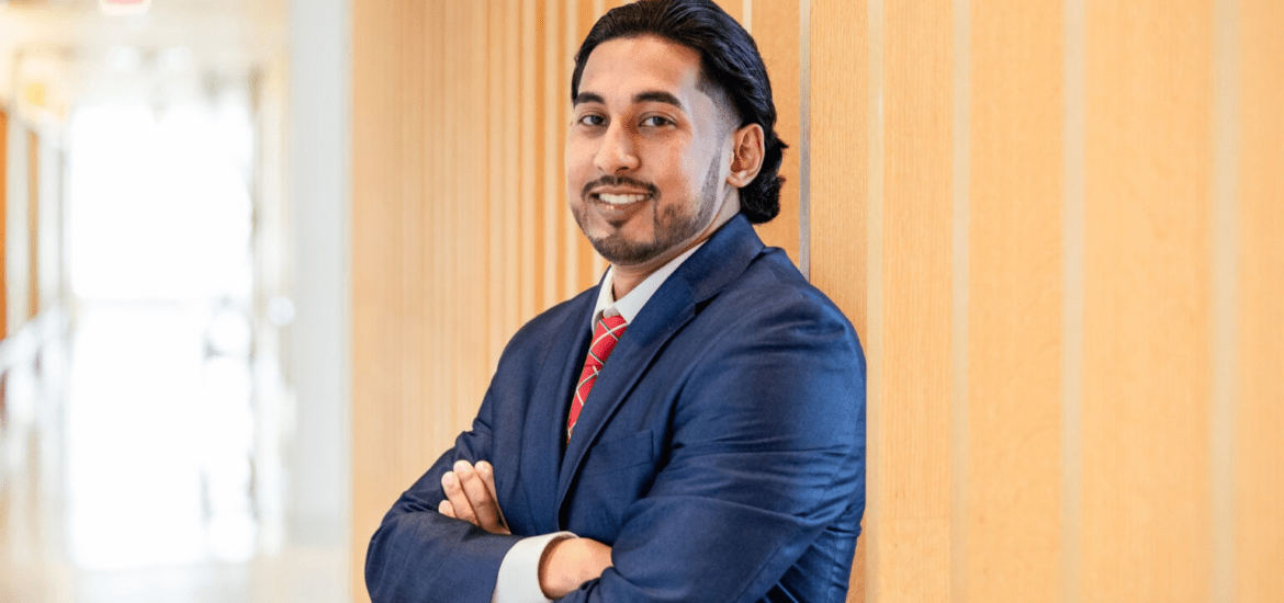 Man in professional business attire standing confidently in a university building hallway.