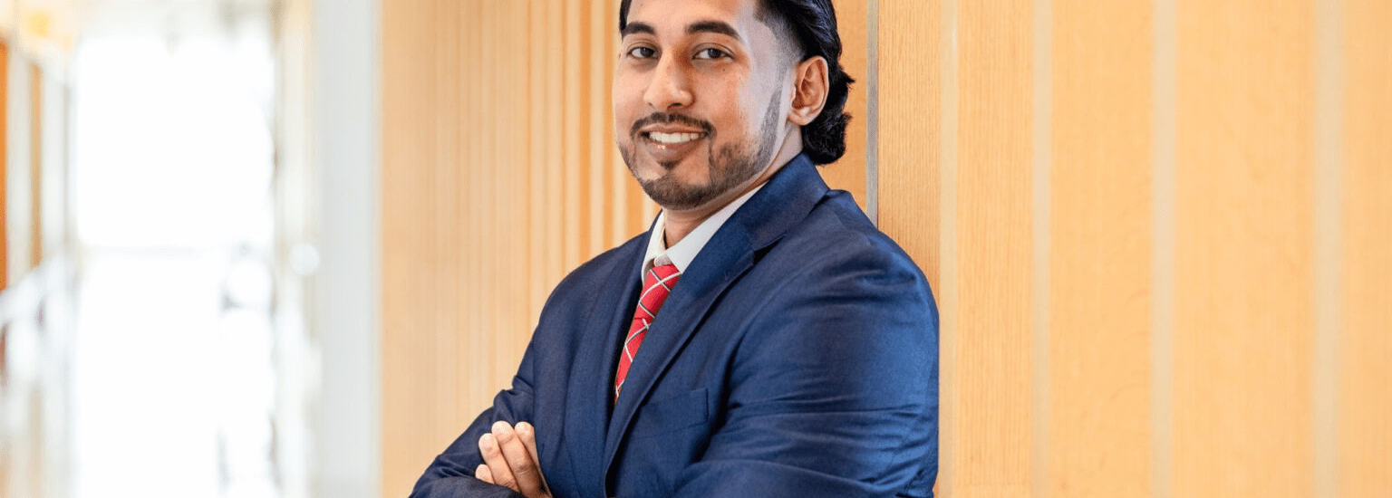 Man in professional business attire standing confidently in a university building hallway.