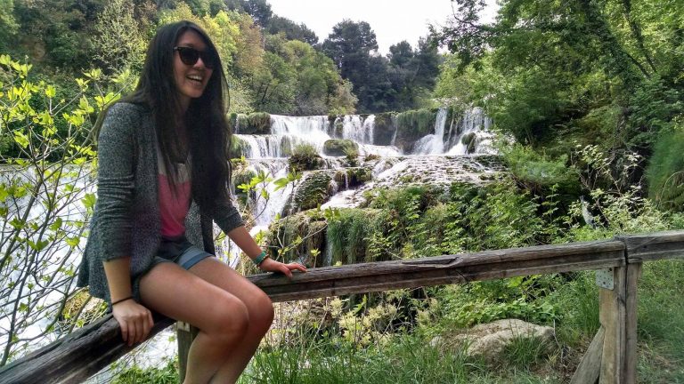 College student sitting near a waterfall while traveling during summer break.