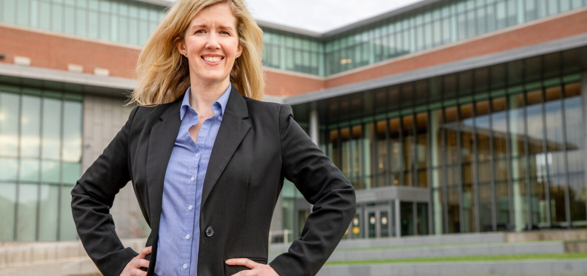 Woman in a dark blazer and blue shirt stands with her hands on her hips outside a Rowan University building.