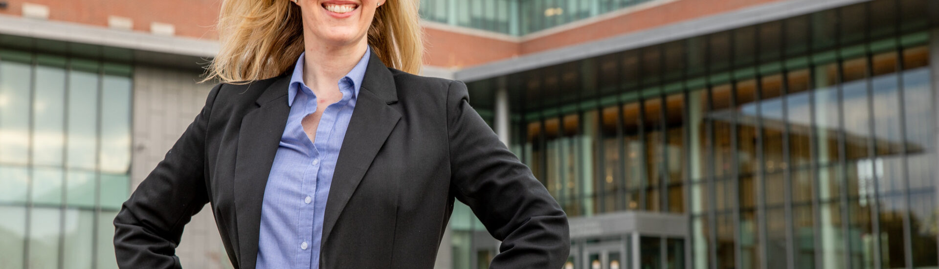 Woman in a dark blazer and blue shirt stands with her hands on her hips outside a Rowan University building.