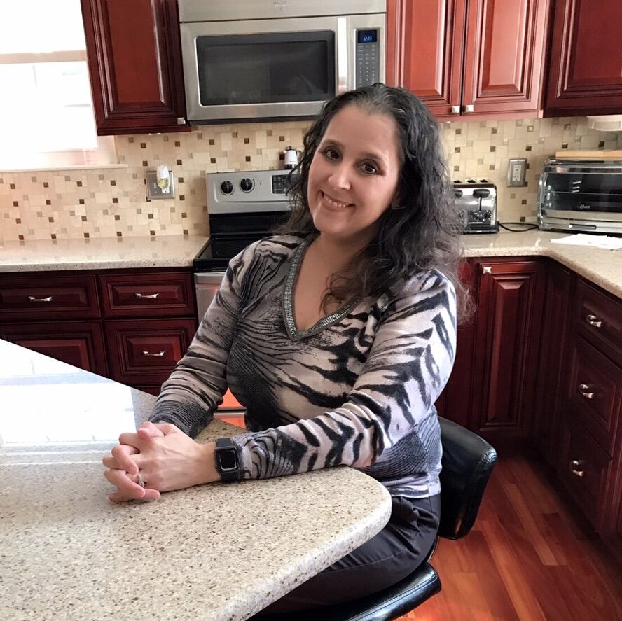 Mom Monica sits at a kitchen table with her hands folded.