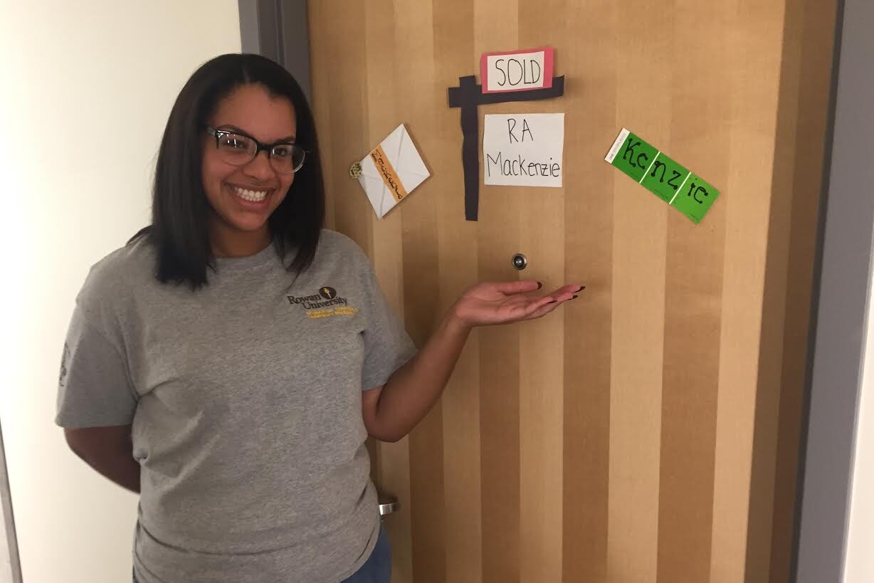 Resident Assistant Mackenzie Brown stands next to her residence hall door adorned with her name.
