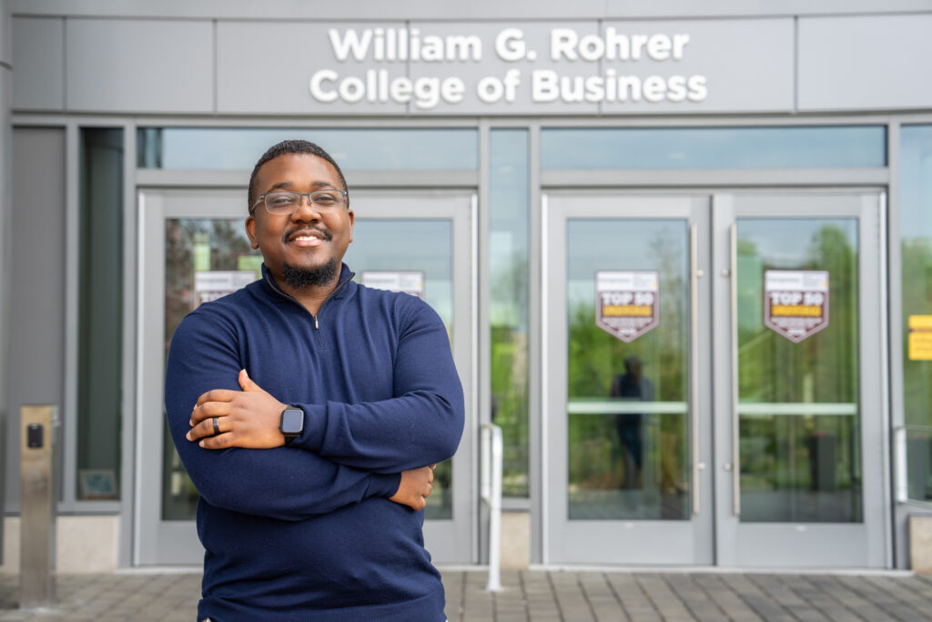 Rowan Online student, Ronald N., smiles with his arms crossed outside the entrance to Rowan University’s William G. Rohrer College of Business.