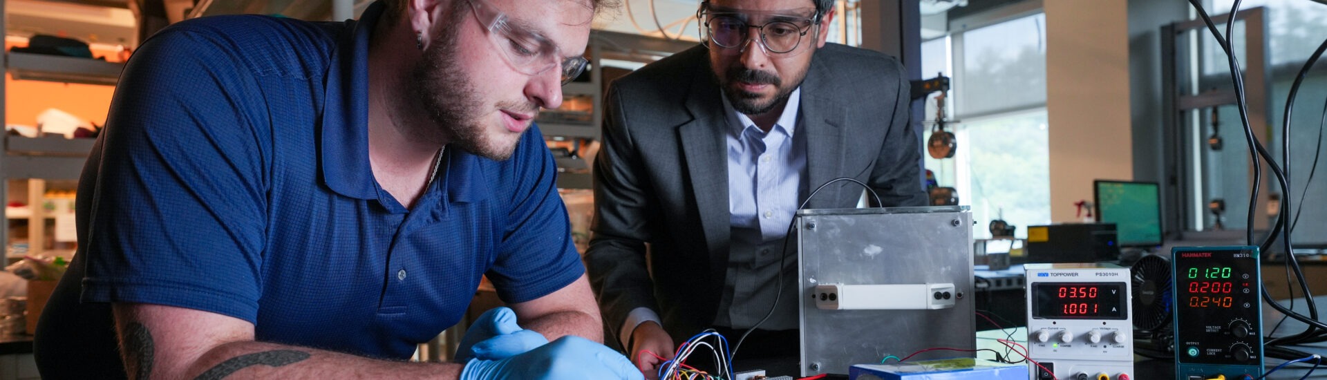 Engineering student and faculty member work together on an electronics project with wires, testing equipment and power supplies in a lab.