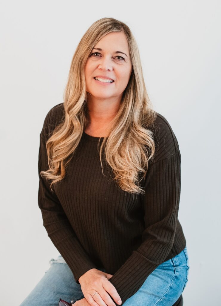 Rowan University online psychology graduate Cindy C. sits on a stool, smiling at the camera and with her hands clasped in her lap. 