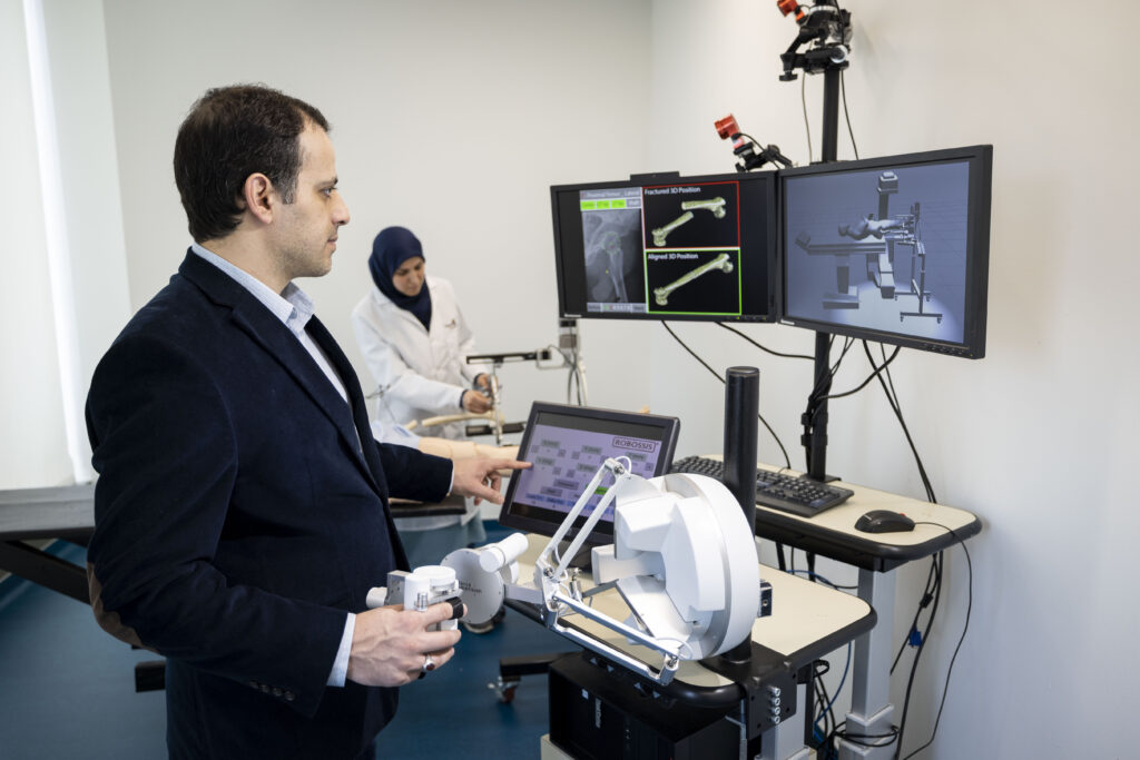 Engineering researcher operating robotic simulation equipment in a lab while viewing 3D models on computer monitors.