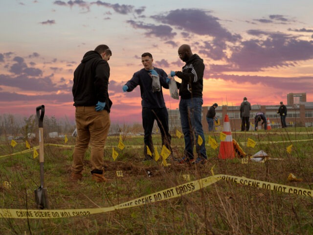 Three emergency response professionals wearing gloves examine a marked outdoor scene behind crime-scene tape while other team members work nearby.