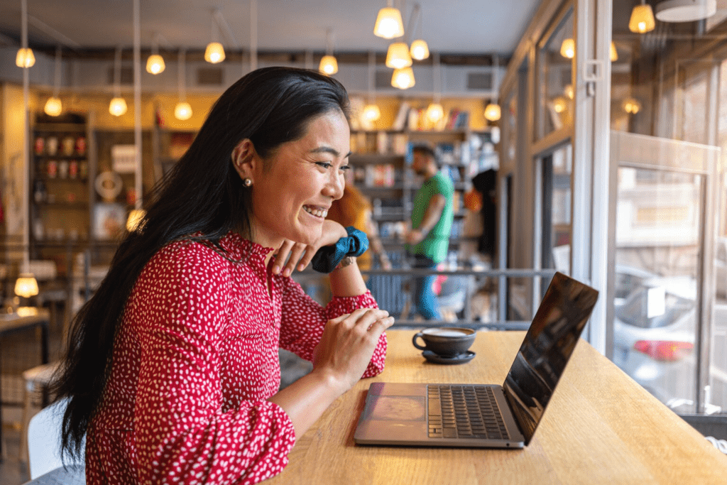 Online business student smiling while using a laptop in a café.