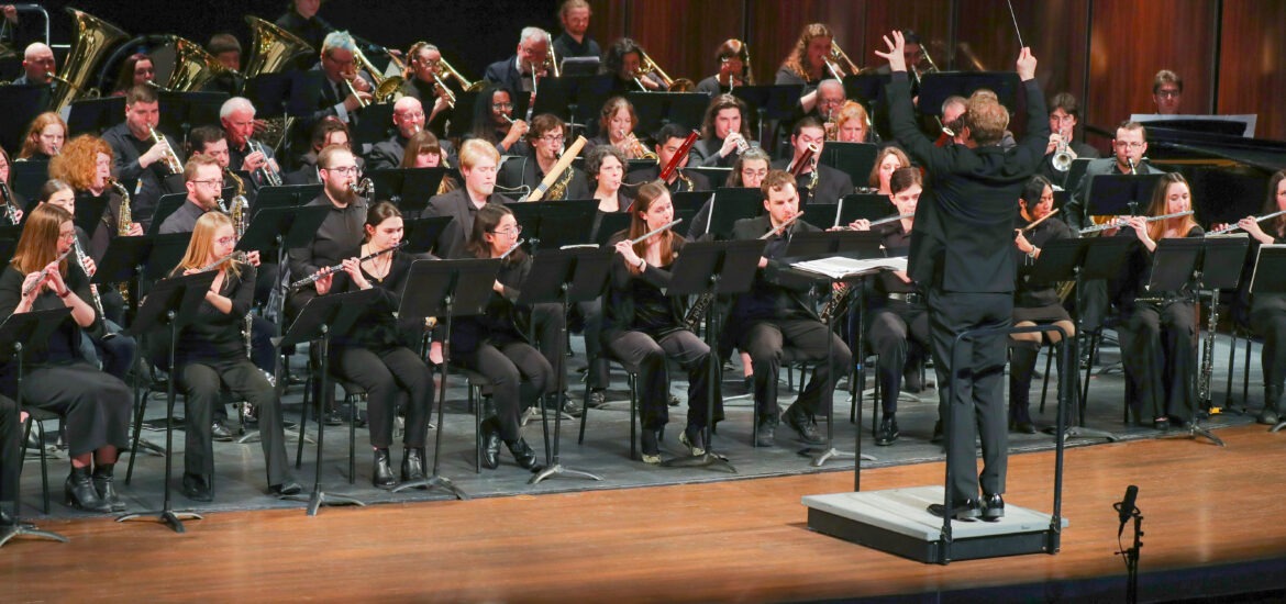 A conductor leads a large orchestra of musicians performing onstage.