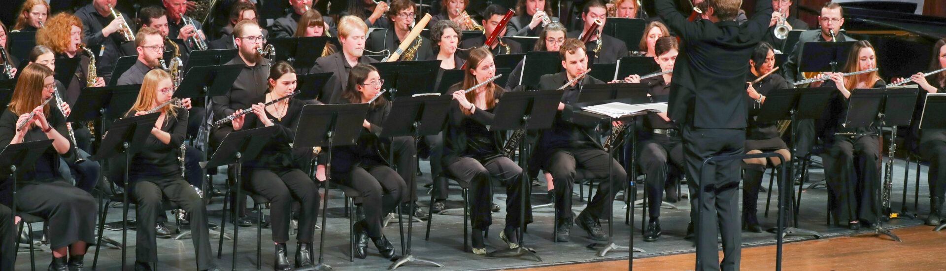 A conductor leads a large orchestra of musicians performing onstage.