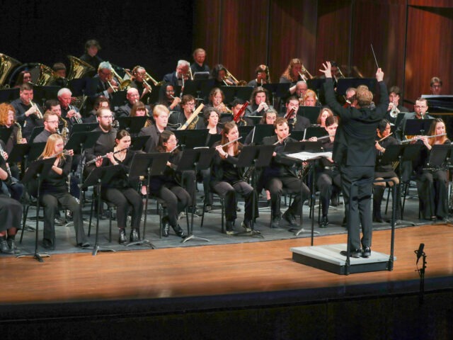 A conductor leads a large orchestra of musicians performing onstage.