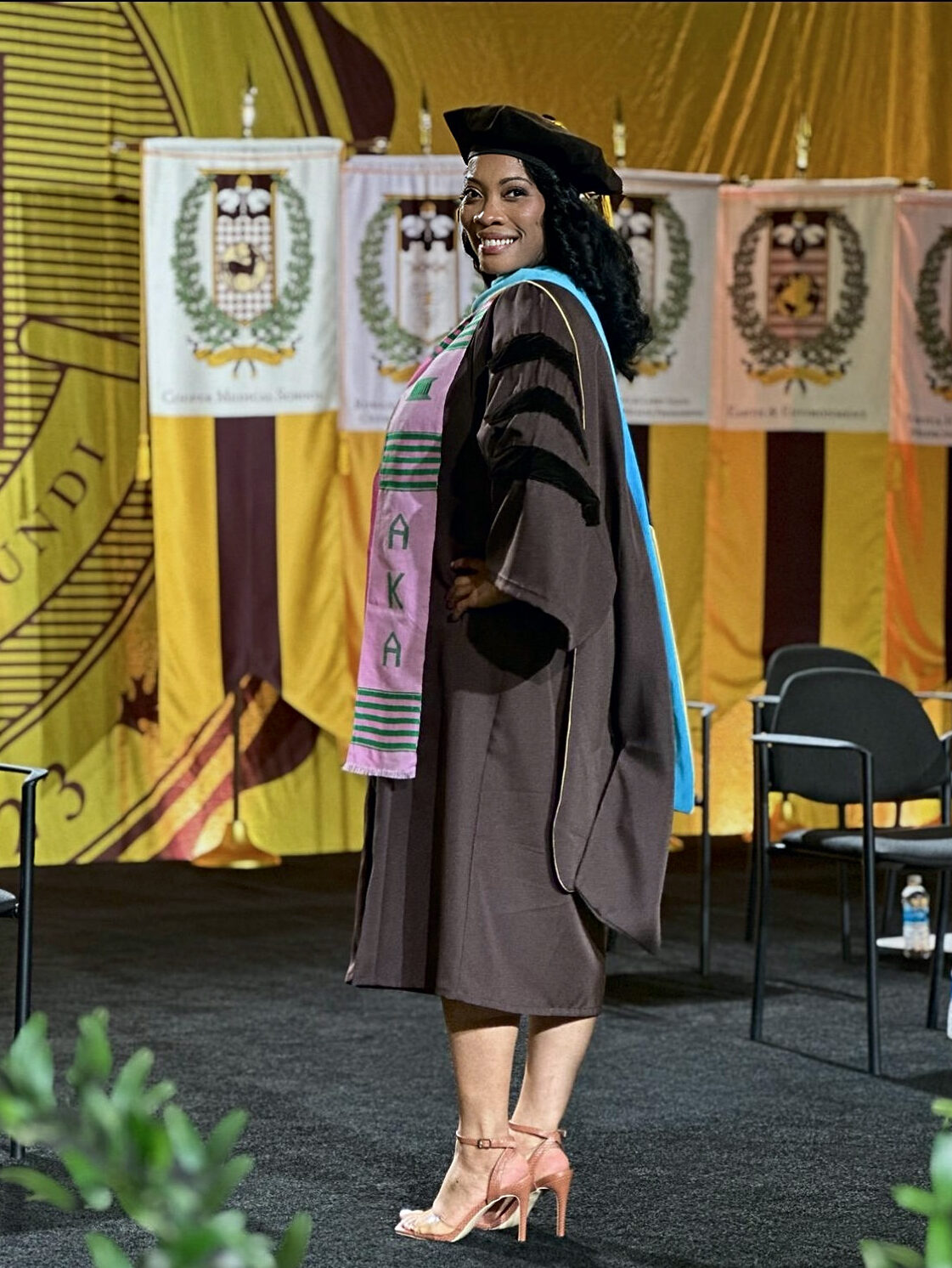 Dr. Clarke smiles onstage in doctoral cap, gown and academic hood.