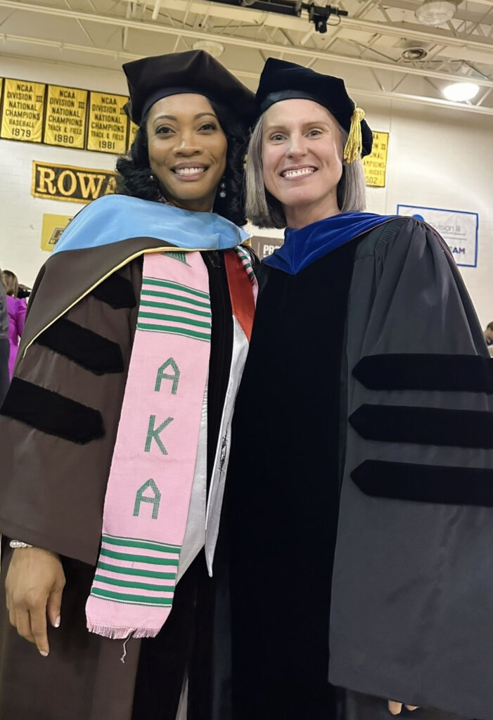 Jametta C. and Dr. Johnson stand together smiling at the camera in academic regalia.