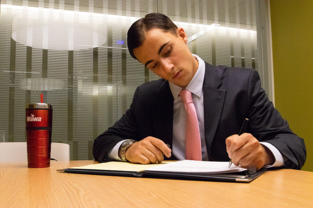 Young professional in a suit writing in a folder at a conference table.