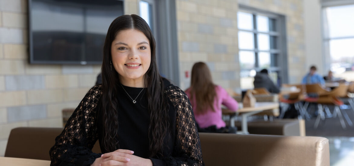 Rowan student smiling while seated at a table in a campus common area.