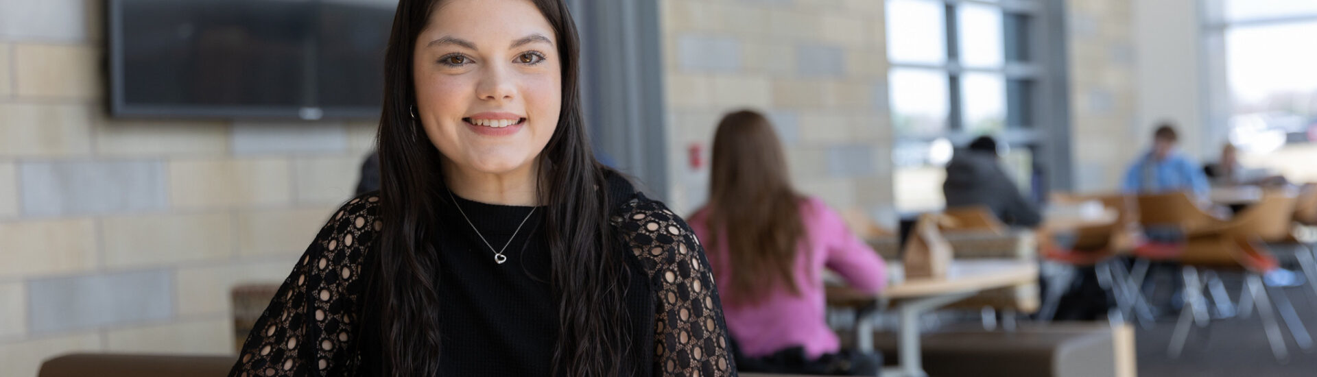 Rowan student smiling while seated at a table in a campus common area.