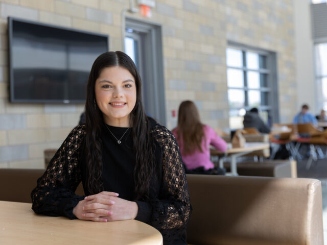 Rowan student smiling while seated at a table in a campus common area.