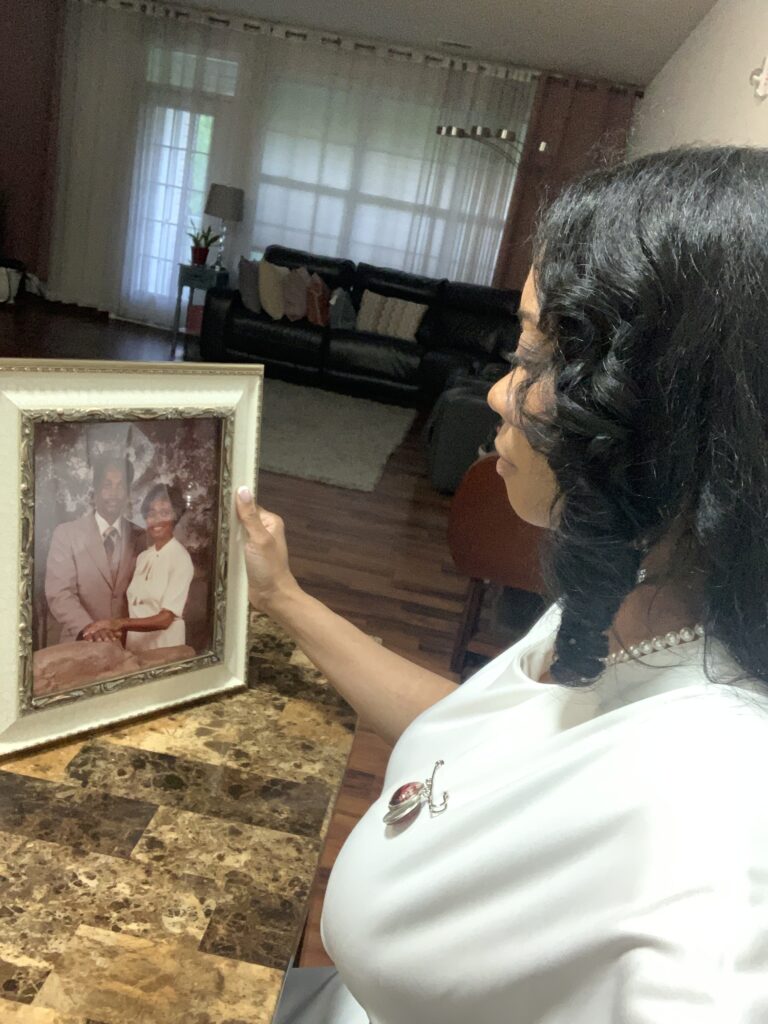 Jametta C. holds a framed photograph of her parents and looks at it.