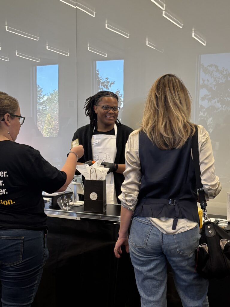 Student speaks with customers across a counter while serving baked goods during a Rowan Roots Market event.